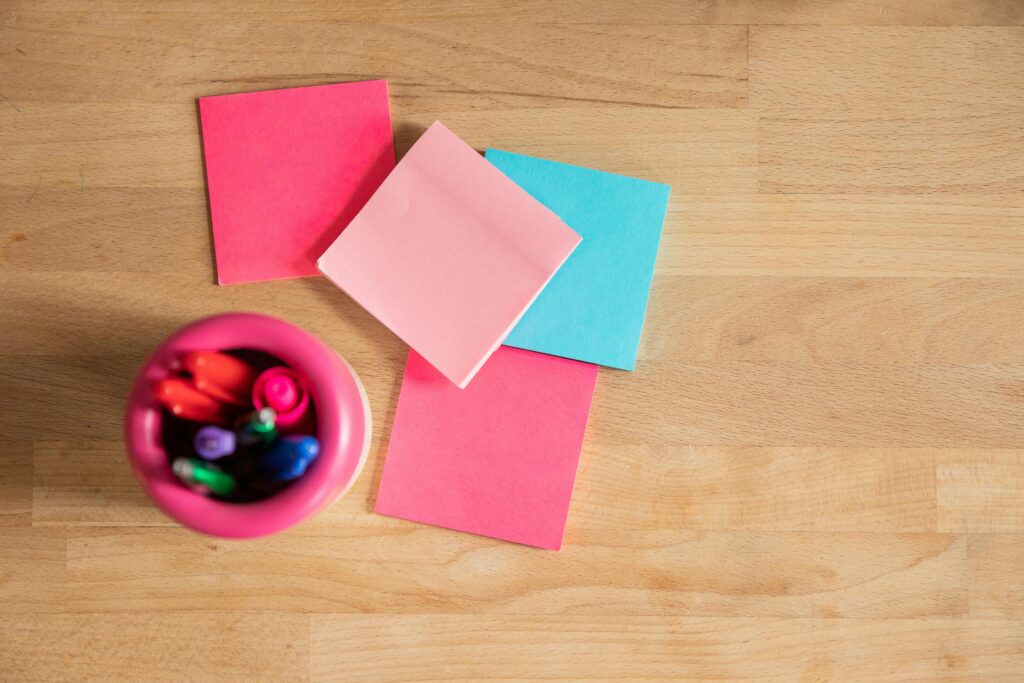 Overhead shot of vibrant sticky notes and pens on a wooden desk.