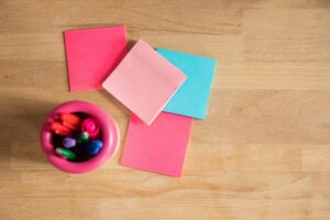 Overhead shot of vibrant sticky notes and pens on a wooden desk.